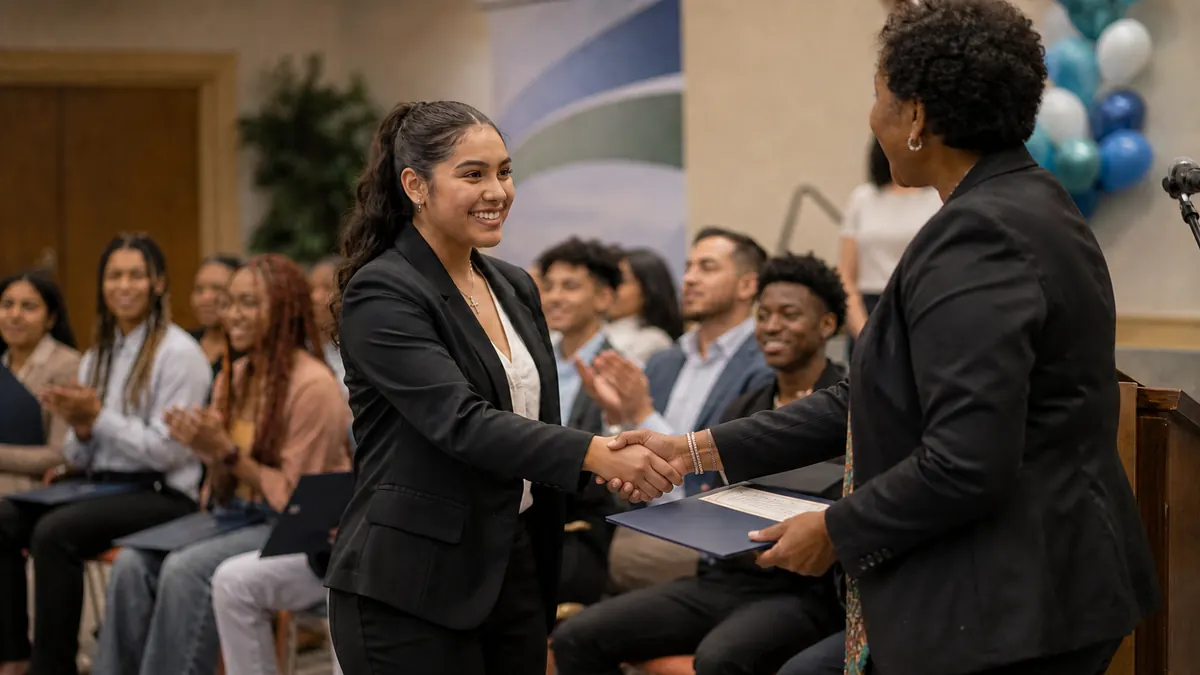 A graduate shaking hands and receiving her certificate at a Skills Nation ceremony, with her cohort applauding behind her.